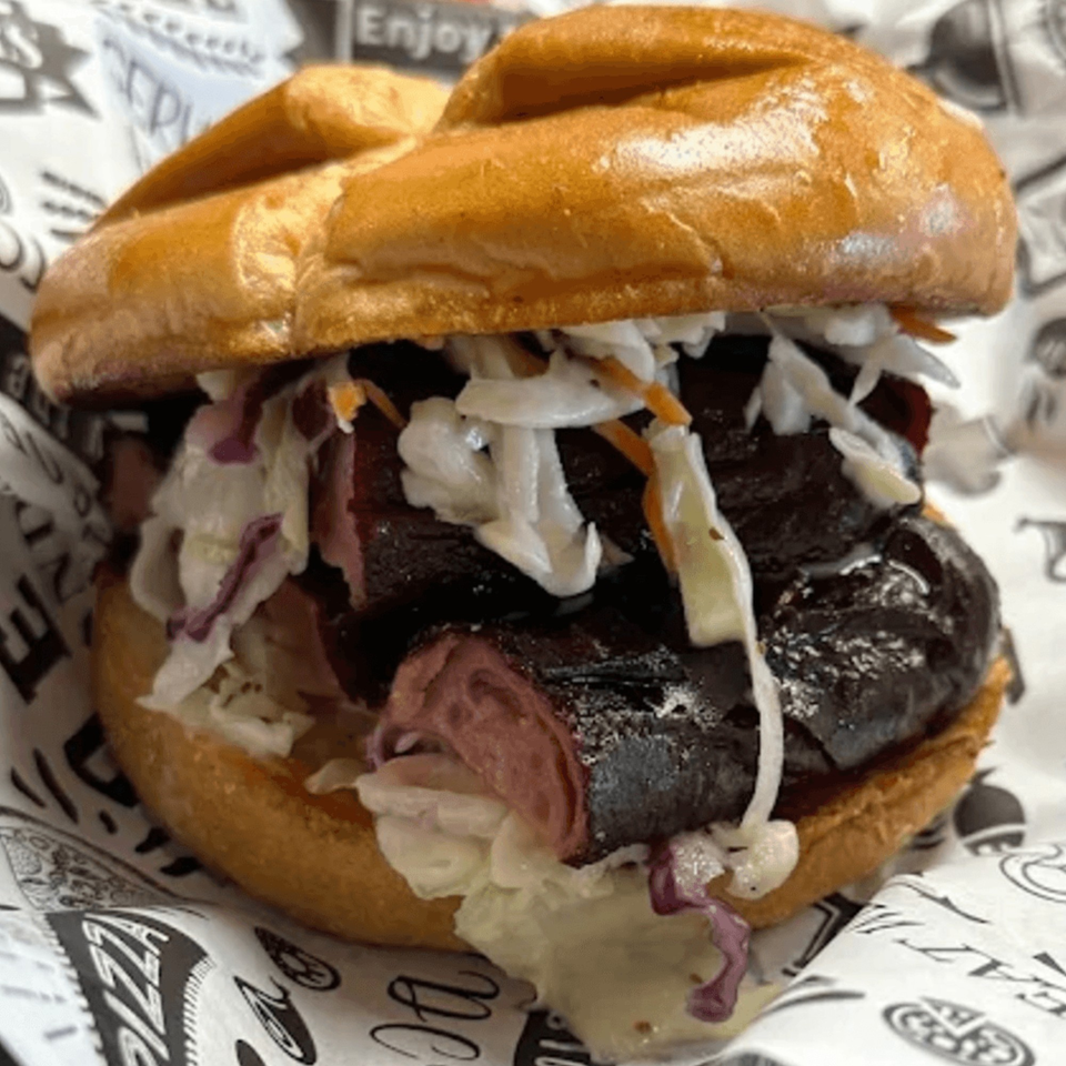 Close-up of a dark fish sandwich with coleslaw on a bun, served on patterned paper.